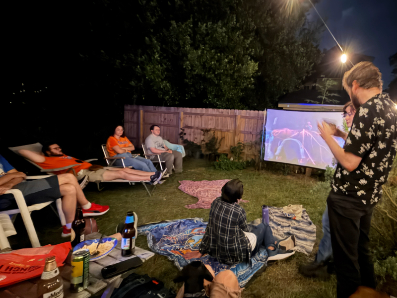 people sitting in a backyard watching a movie on a projector